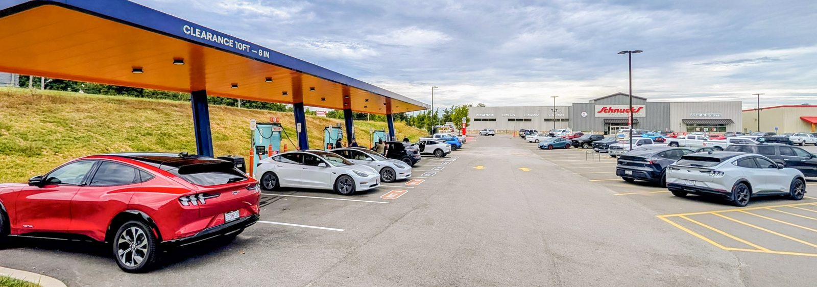 A red Mustang Mach-E and two white Teslas charging under the IONNA canopy, with the Schnucks store across the lot