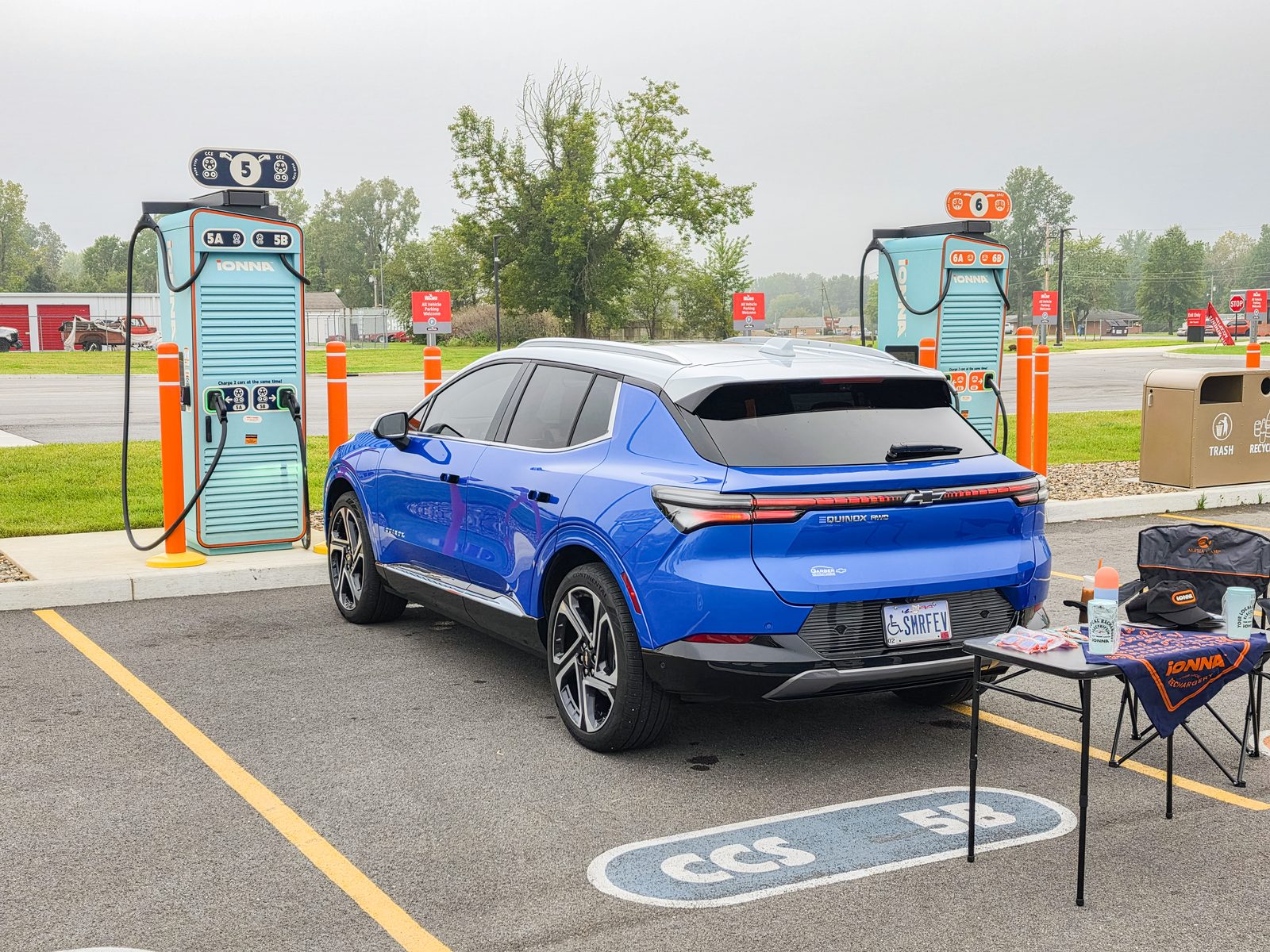 A blue Chevrolet Equinox EV charging beside a host's table laid out with IONNA swag