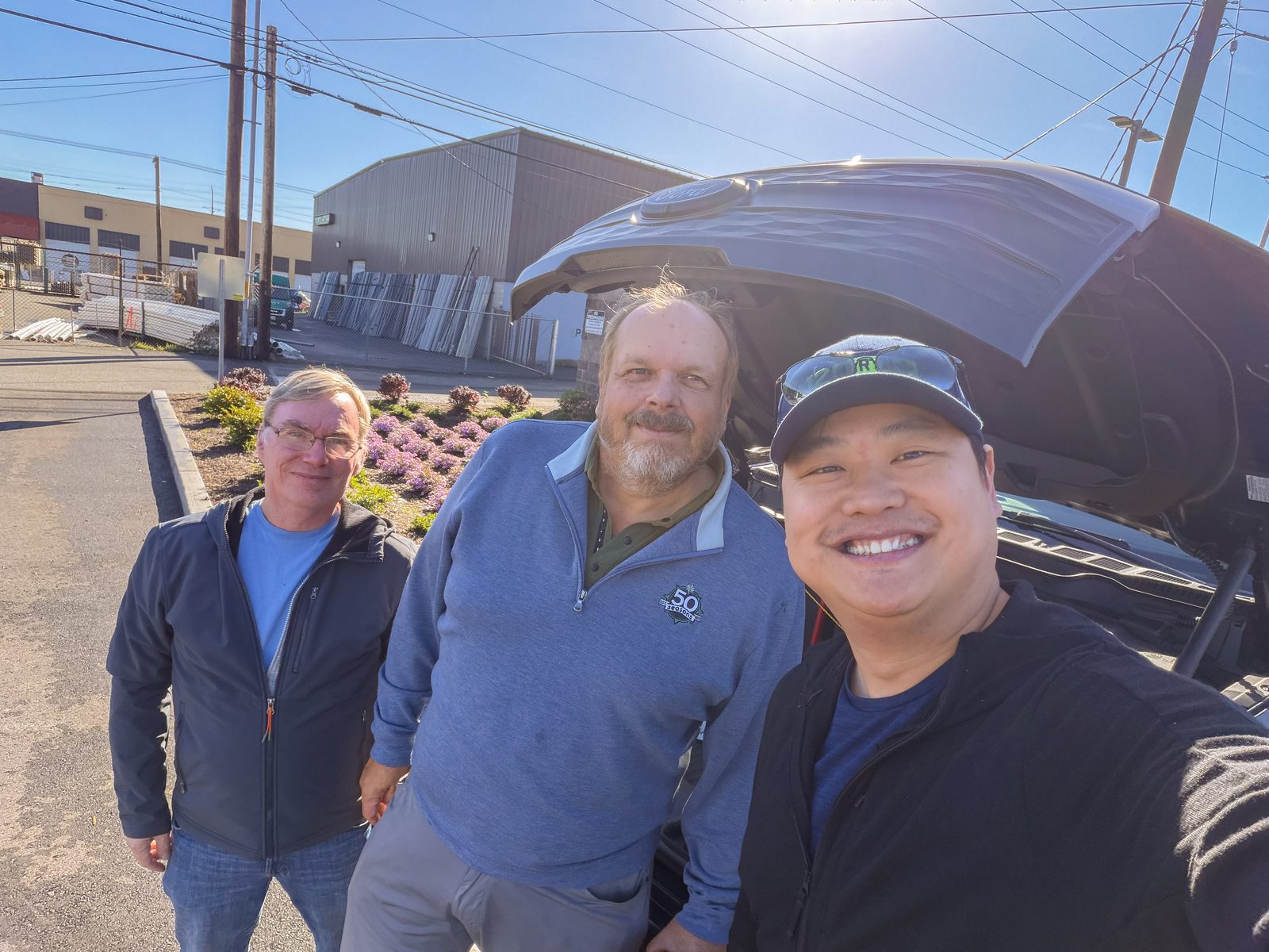 Three drivers smiling for a photo beside an EV with its hood open