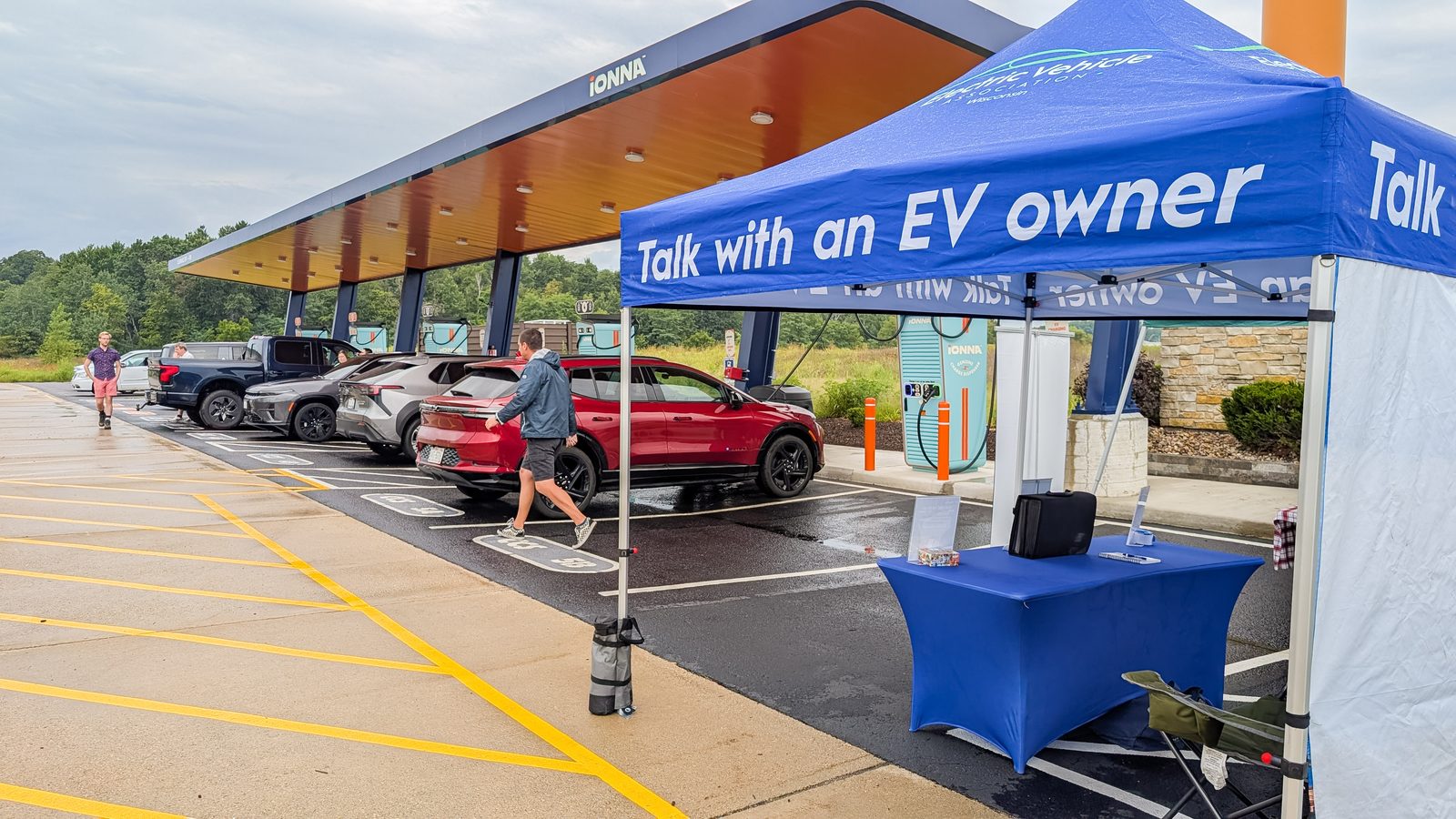A Talk with an EV owner tent set up beside the chargers, with a red Blazer EV and others under the canopy